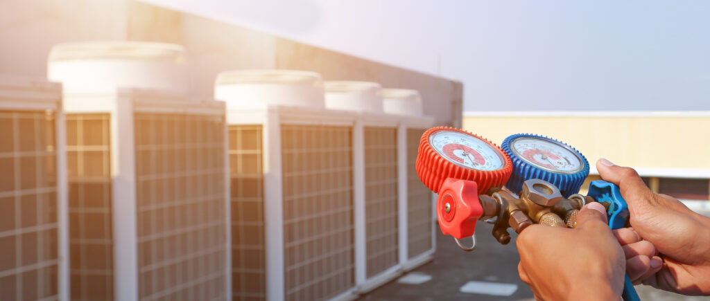 Technician using manifold gauge is measuring equipment for filling industrial factory air conditioners after cleaning and checking for maintenance outdoor air compressor unit.