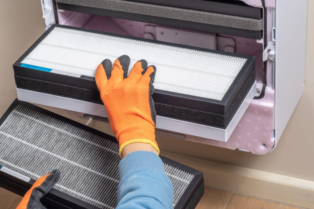 A technician in orange gloves replacing a HEPA filter in an HVAC system to improve indoor air quality in Ashland, KY homes and businesses.